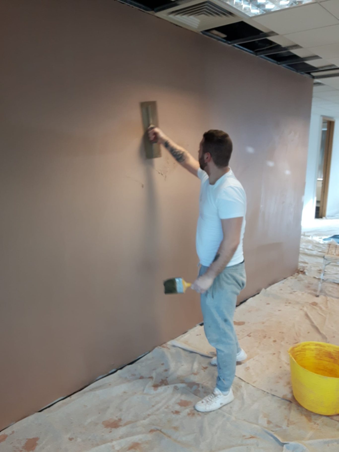 A person applying plaster to a wall in an interior space.